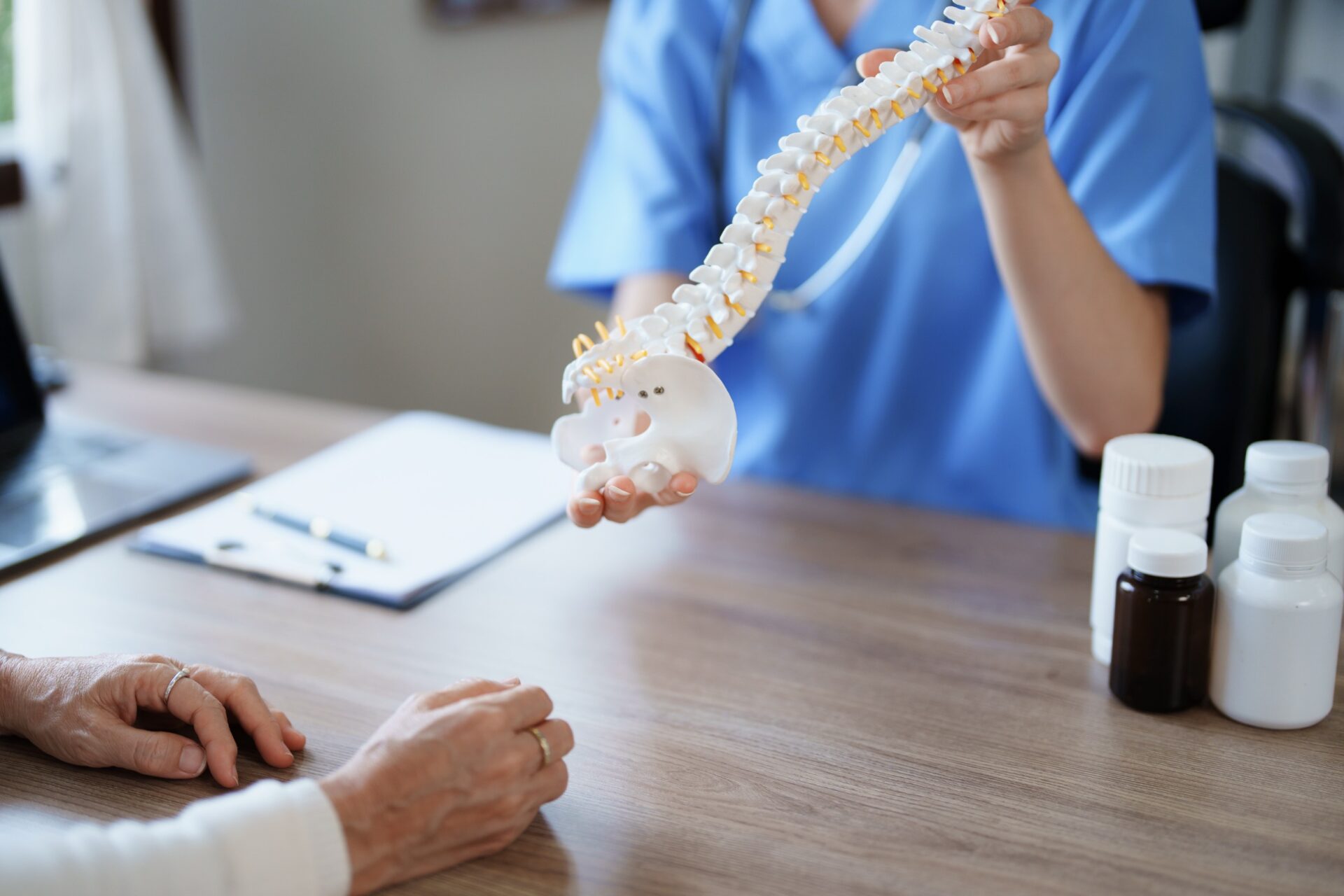 Female doctor holding a model of the spine and explaining it to an elderly woman