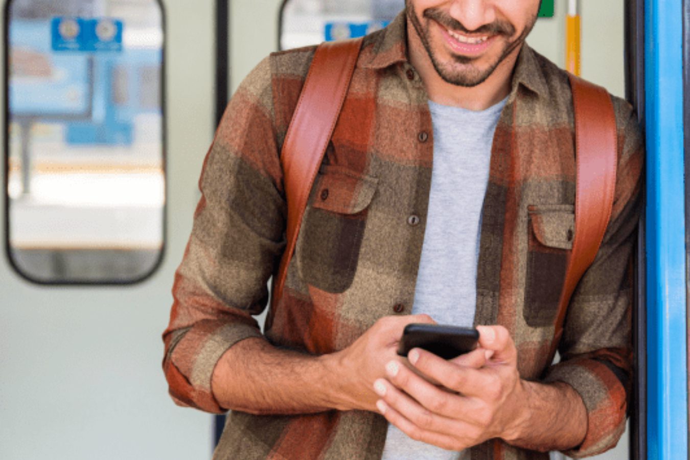 A man stands on a train, holding a cell phone, engaged in conversation or browsing content on the device.